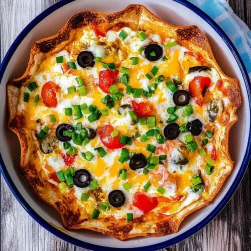 Freshly baked breakfast tortilla quiche with golden edges in a round ceramic dish with eggs, cheese, and vegetables